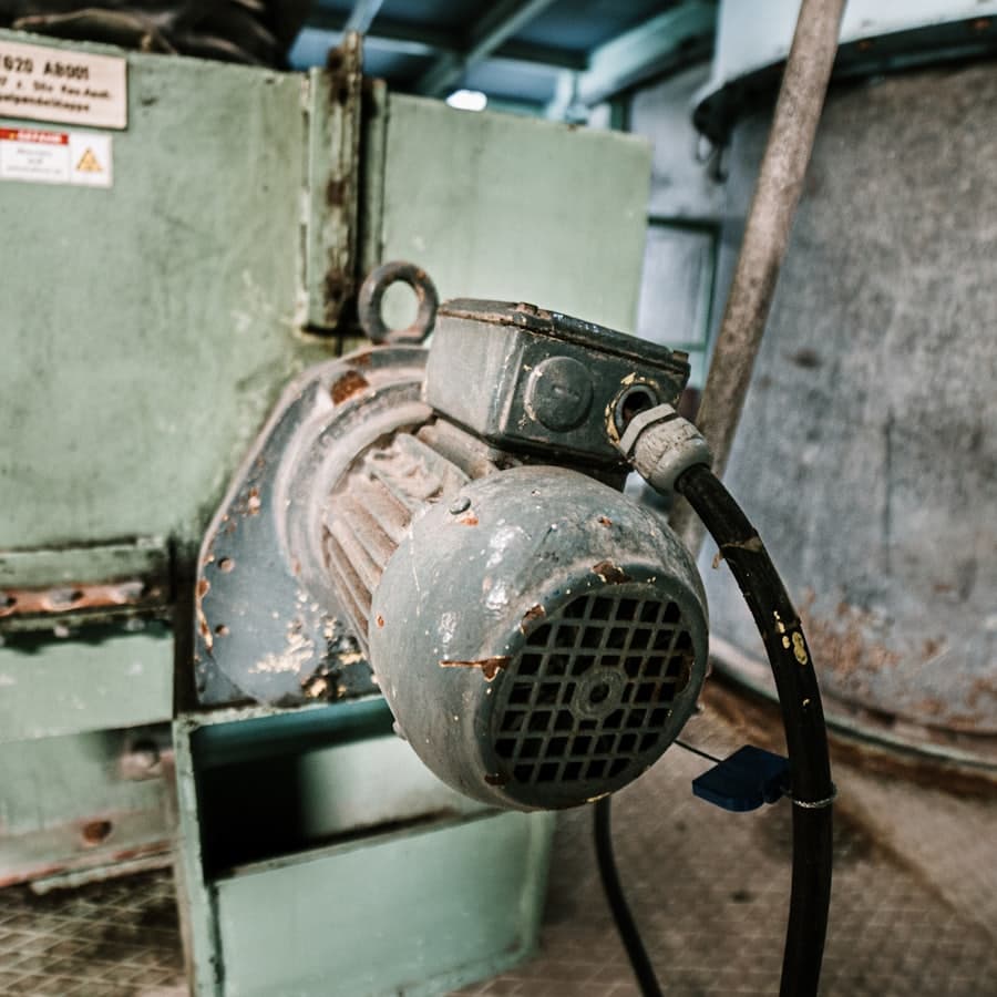 A weathered industrial electric motor mounted to a pump on a plant floor.