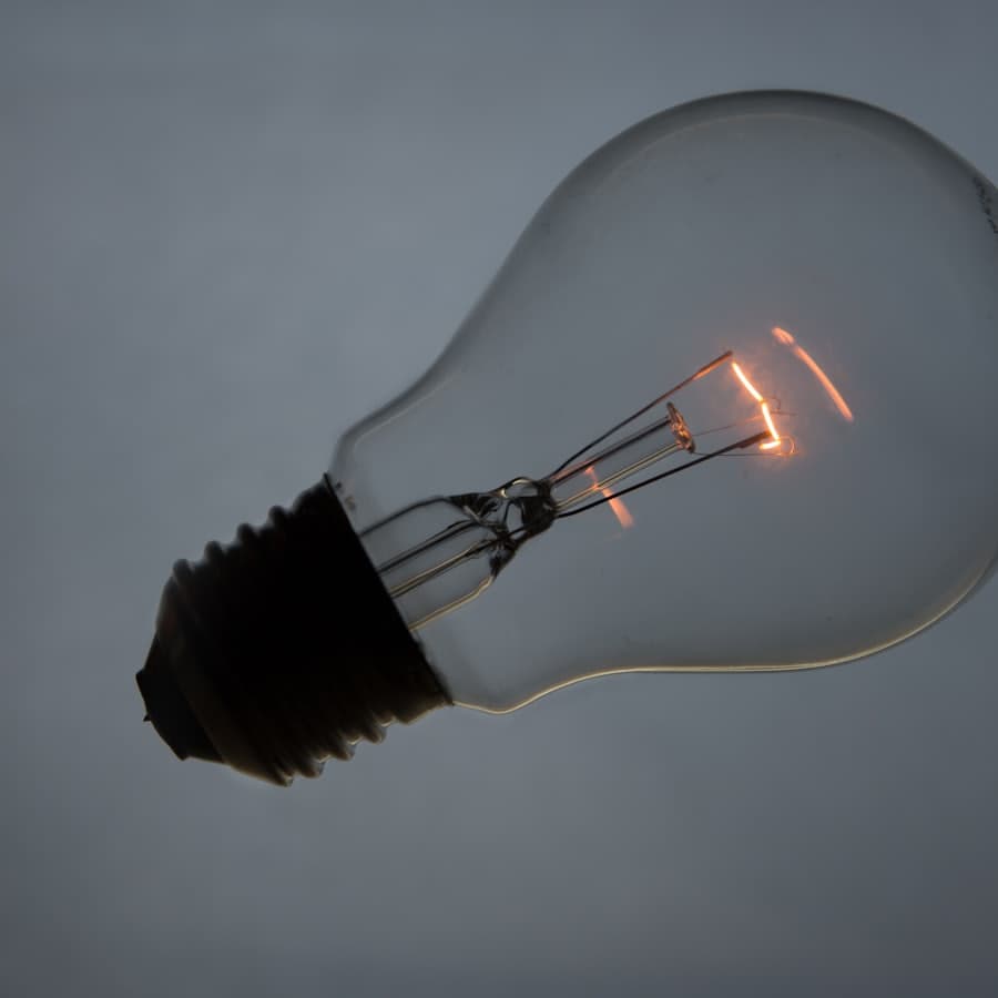 An incandescent light bulb with its filament glowing orange against a gray background.